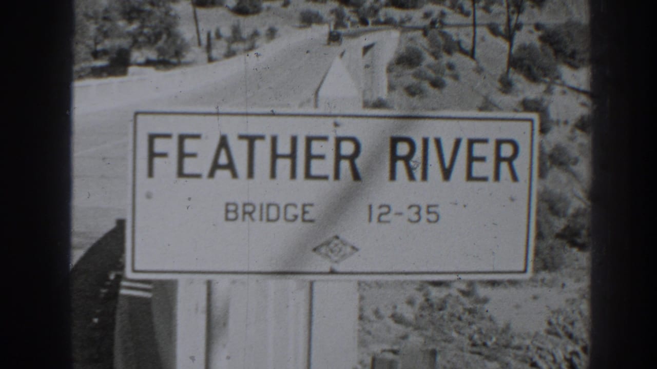 White roadside sign reading Feather River Bridge 12-35 beside a road and dry landscape.