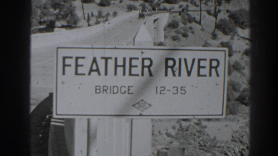 1938 Orovilla, California frame showing a Feather River Bridge sign with a road and arid hillside in the background.