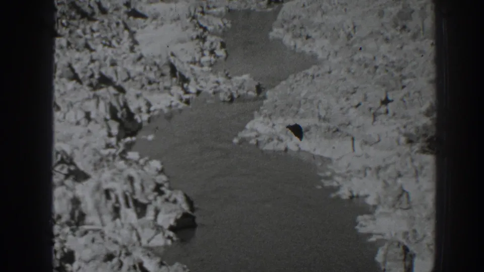 1938 Oroville-area home-movie frame showing a narrow creek bordered by rough rock, dirt banks, and sparse vegetation.