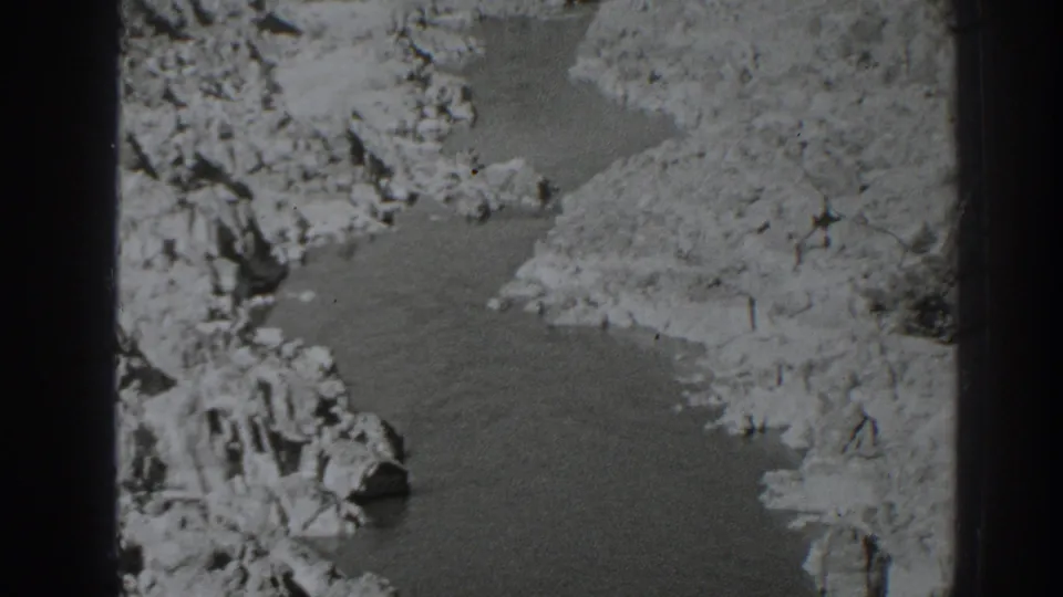 Late-1930s black-and-white frame of a creek bend in rocky Oroville terrain, seen from a steady home-movie viewpoint.