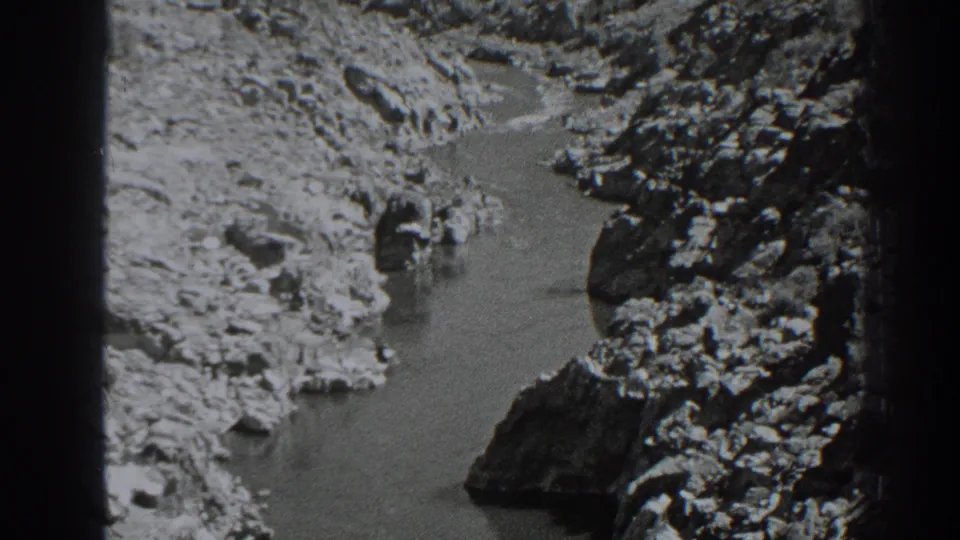 Vintage 8mm frame of the Oroville river scene, with pale canyon rocks and darker boulders around the water.