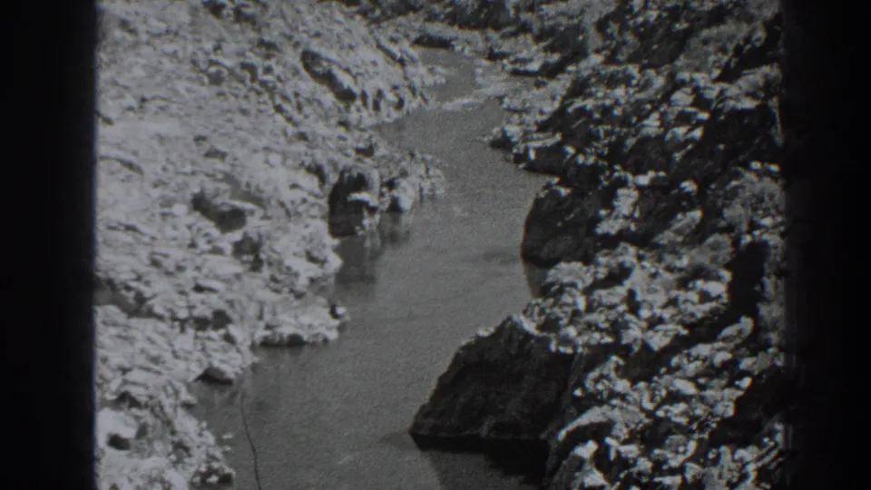 Black-and-white 8mm view of a narrow watercourse bordered by rough rock and dry ground in the Oroville area.