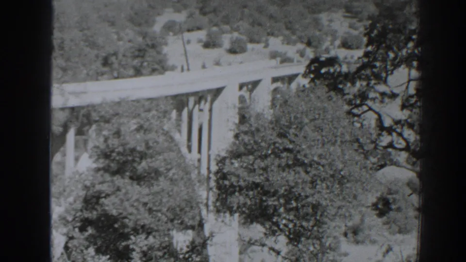 1938 Oroville-area home-movie frame showing a concrete bridge spanning a brushy canyon with trees in the foreground.