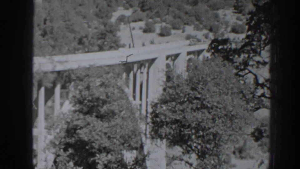 Archival 8mm view near Oroville showing a bridge with vertical supports, trees, and dense brush below.