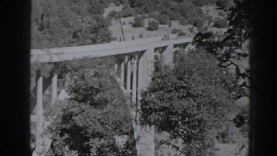 1938 Oroville-area 8mm frame showing a car on an elevated concrete bridge surrounded by wooded slopes.