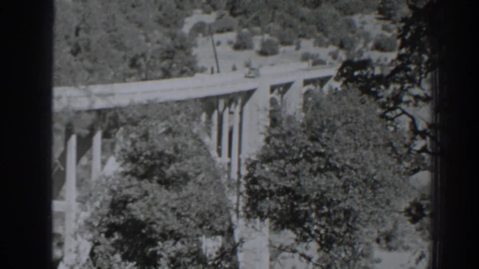 Black-and-white 1938 Oroville frame with a long concrete bridge, vertical piers, and dense trees below.