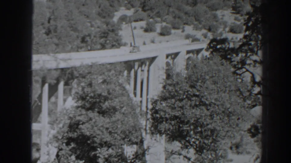 1938 Oroville home-movie frame showing the bridge from above, partly obscured by foreground film edges and trees.