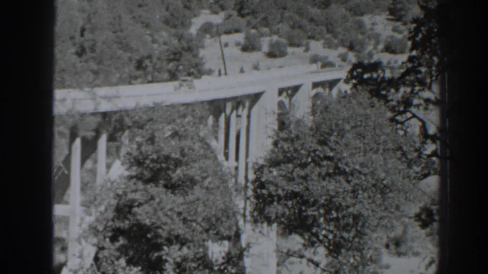 Final 1938 Oroville frame of a tall concrete bridge set into a forested landscape, seen from an elevated home-movie viewpoint.
