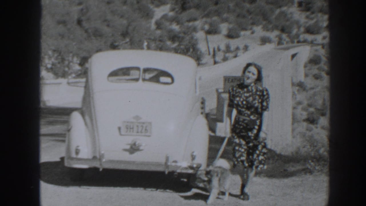 Woman in a patterned dress poses by a classic car and Feather River sign in the stated 1938 Oroville, California footage.