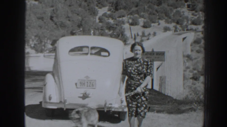 Classic car rear, visible plate, woman, and small dog appear beside the Feather River sign in 1938 Oroville travel footage.