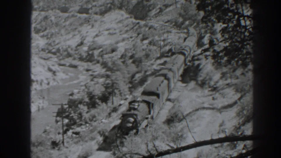 The train continues through the Oroville mountain pass, with freight cars following a curved track through snow and sparse trees.