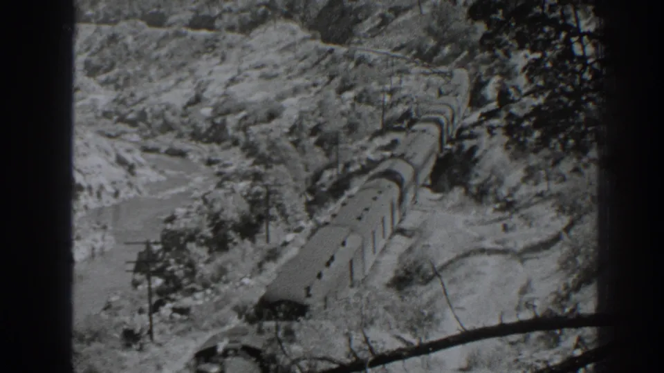 A long line of freight cars moves through the snowy Oroville landscape, seen from a high handheld 8mm viewpoint.