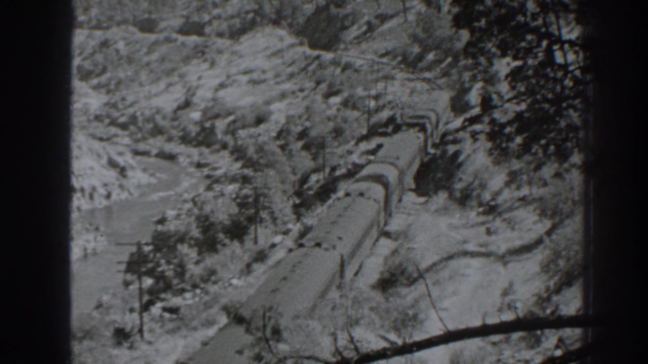 1938 Oroville-area home-movie frame showing a freight train on curving tracks through rocky terrain beside a river or watercourse.