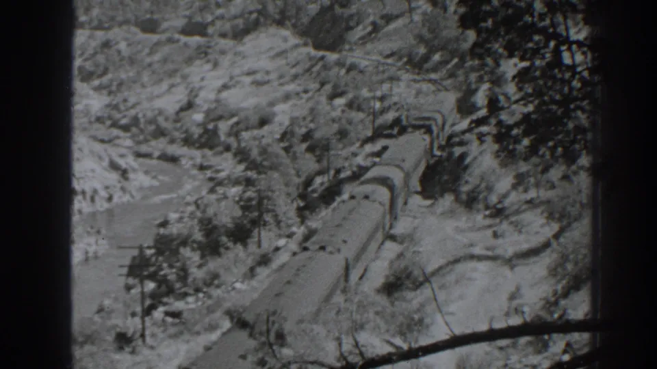 1938 Oroville-area home-movie frame showing a freight train on curving tracks through rocky terrain beside a river or watercourse.