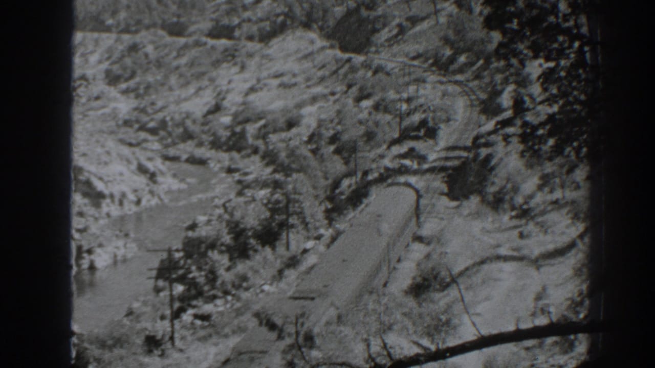 Distant rail or road corridor beside river water in a rocky valley.