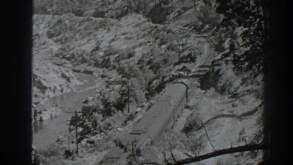 1938 Oroville-area 8mm frame showing a winding corridor beside water, rocky slopes, trees, and utility poles.