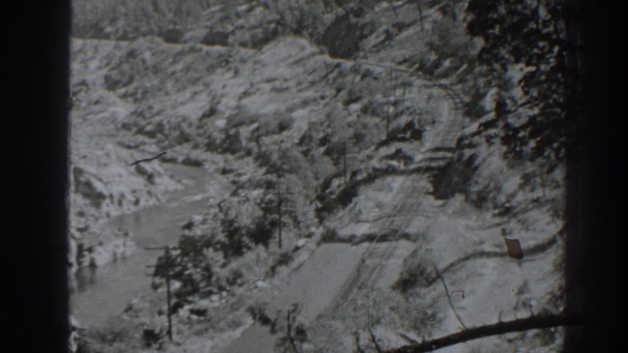 1938 Oroville-area view of a curving rail or road line through rocky terrain, with branches at the edge of the frame.