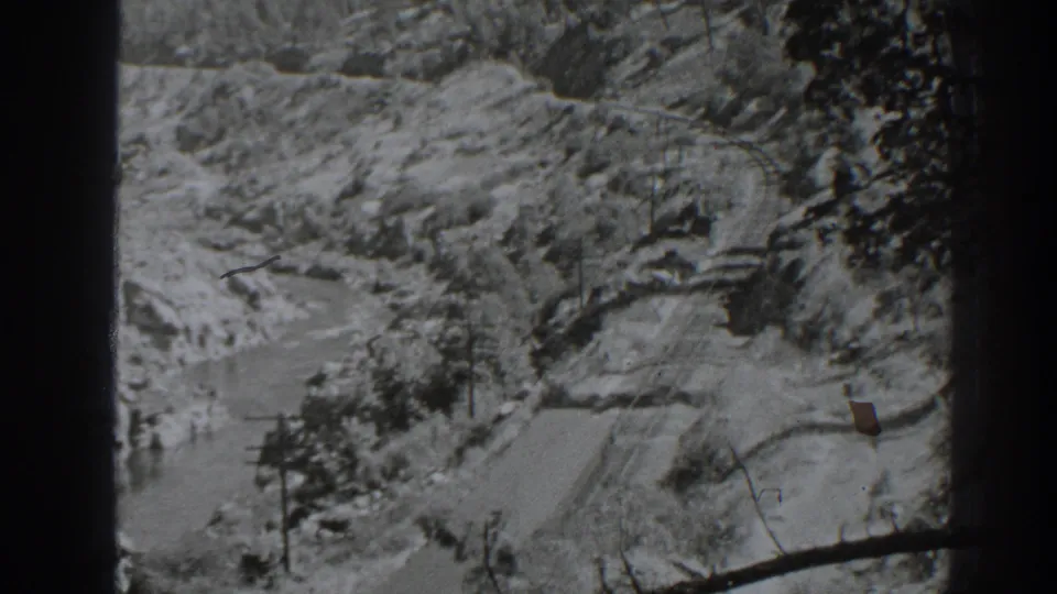 1938 Oroville-area view of a curving rail or road line through rocky terrain, with branches at the edge of the frame.