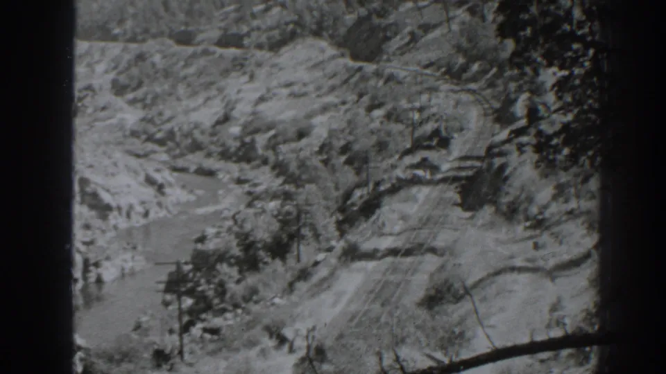 Black-and-white 8mm frame from Oroville showing a river bend, utility poles, and a winding route through a rugged valley.