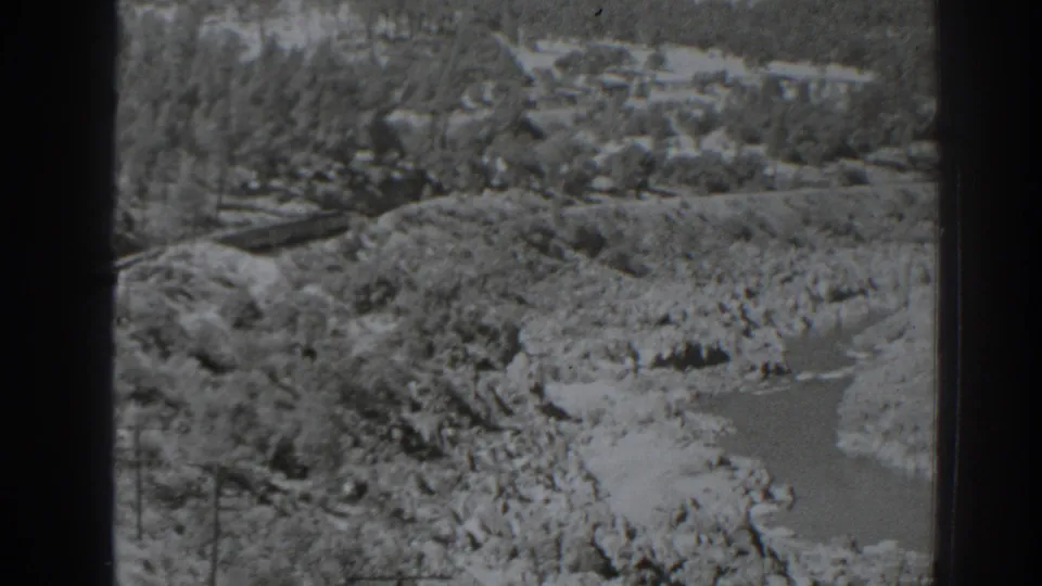 1938 Oroville, California home-movie frame showing a river through rocky terrain, wooded hillsides, and a rail line on the left.