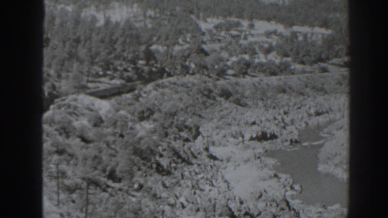 1938 Oroville, California frame with a river and rocky banks below a wooded hillside, with a train visible near the left edge.