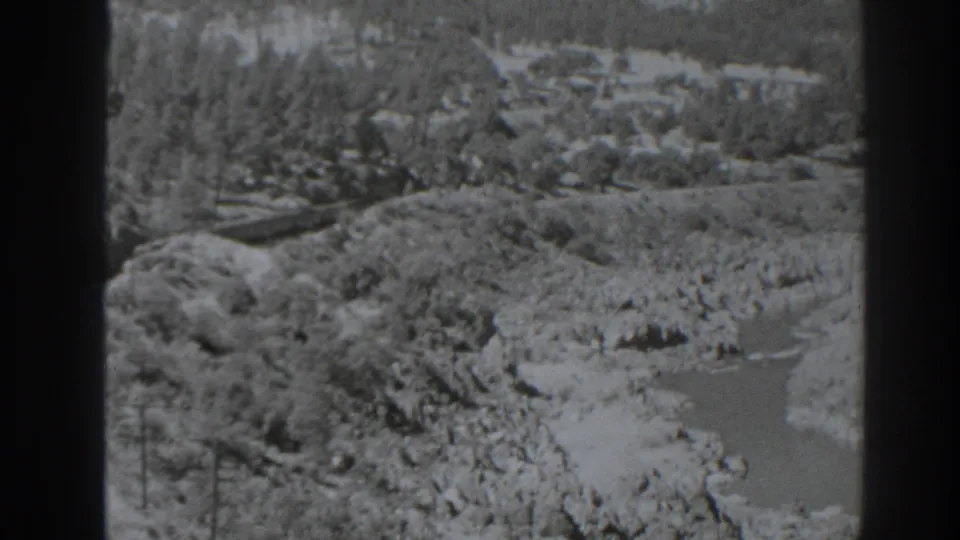 1938 Oroville, California frame with a river and rocky banks below a wooded hillside, with a train visible near the left edge.