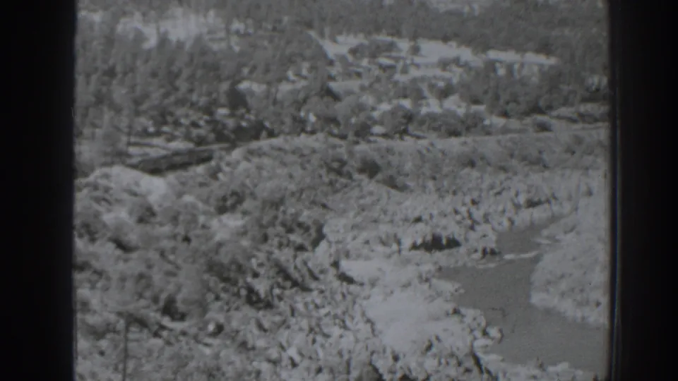 Black-and-white 1938 Oroville-area view of a rocky river or wash below wooded hills, framed by 8mm film borders.