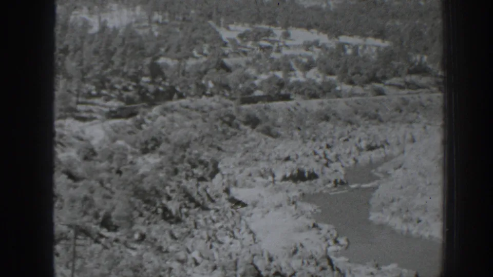 Black-and-white home-movie frame of rocky banks, a pale channel, and wooded slopes near Oroville in 1938.