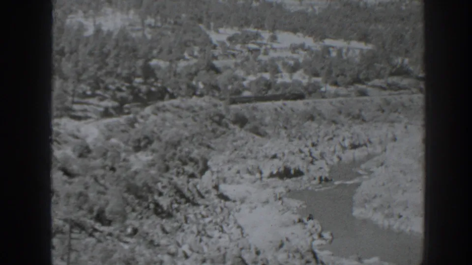 1938 Oroville-area 8mm still with a rocky channel, scrub-covered banks, and wooded hills in soft black-and-white detail.