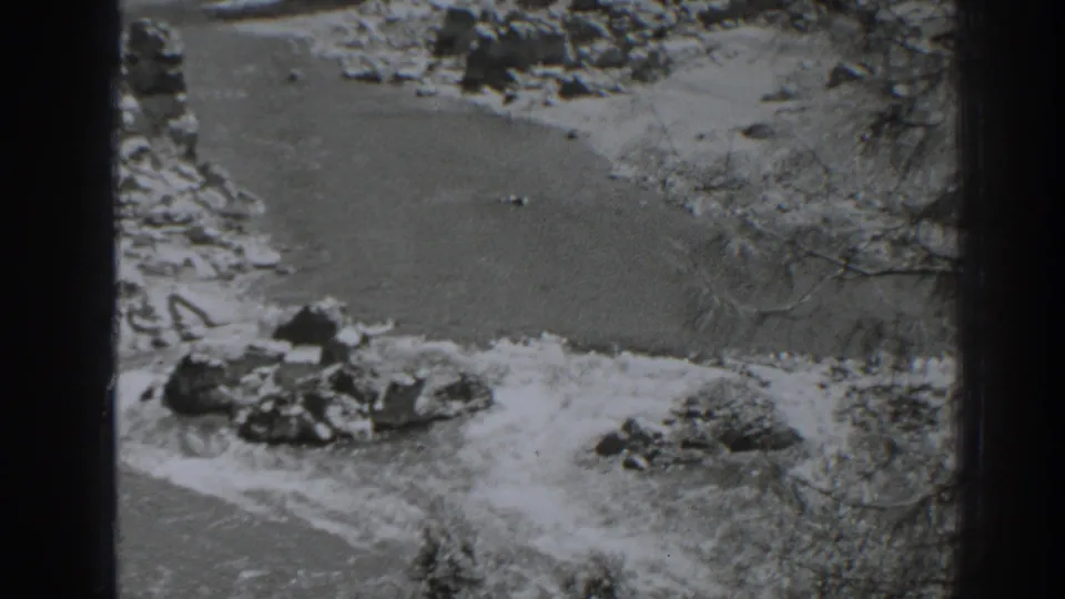 Final black-and-white 8mm frame of the Oroville river scene, with rocks, water, and trees viewed from above.