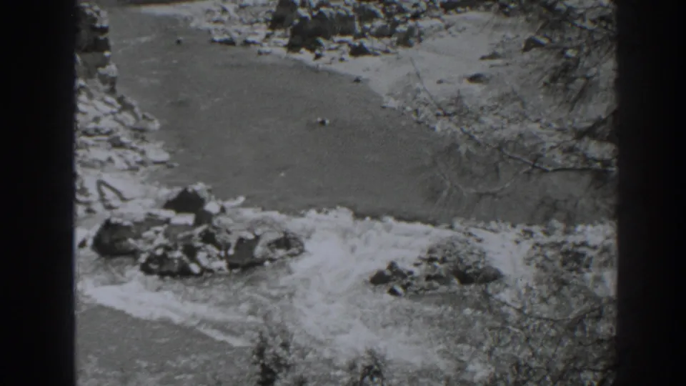 Black-and-white 8mm frame of the Oroville river canyon with turbulent water and exposed rocks.