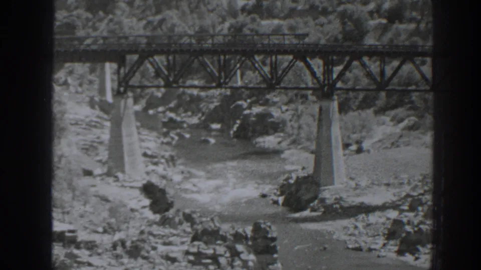 1938 Oroville 8mm frame showing a steel truss bridge over a rocky river channel.
