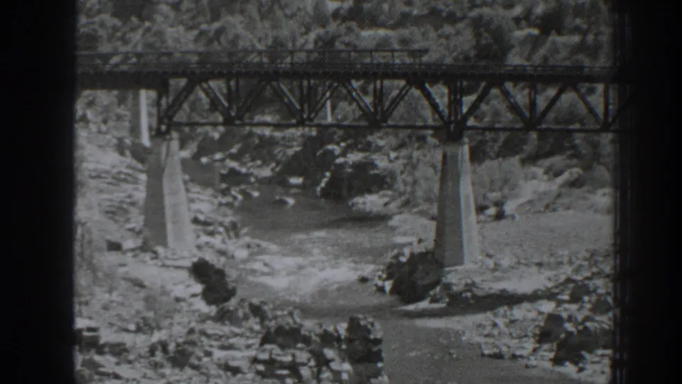 Black-and-white Oroville frame with a steel rail bridge over rushing water and rocks.