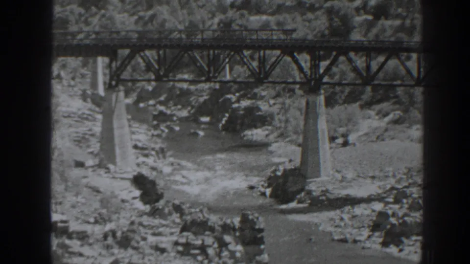 1938 Oroville, California home-movie frame showing a steel railroad bridge spanning fast water and rocks below.