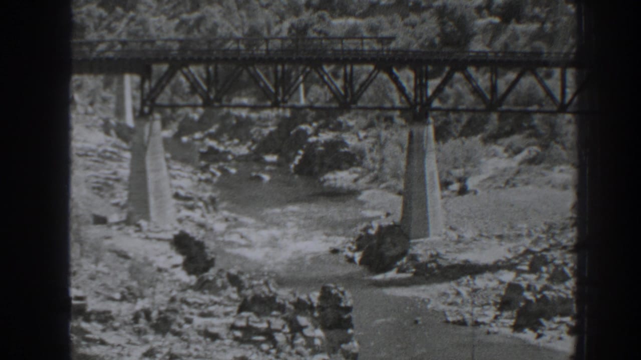 Black-and-white 8mm view of the Oroville railroad bridge with concrete piers set in a rocky riverbed.