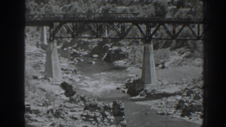 Black-and-white 8mm view of the Oroville railroad bridge with concrete piers set in a rocky riverbed.