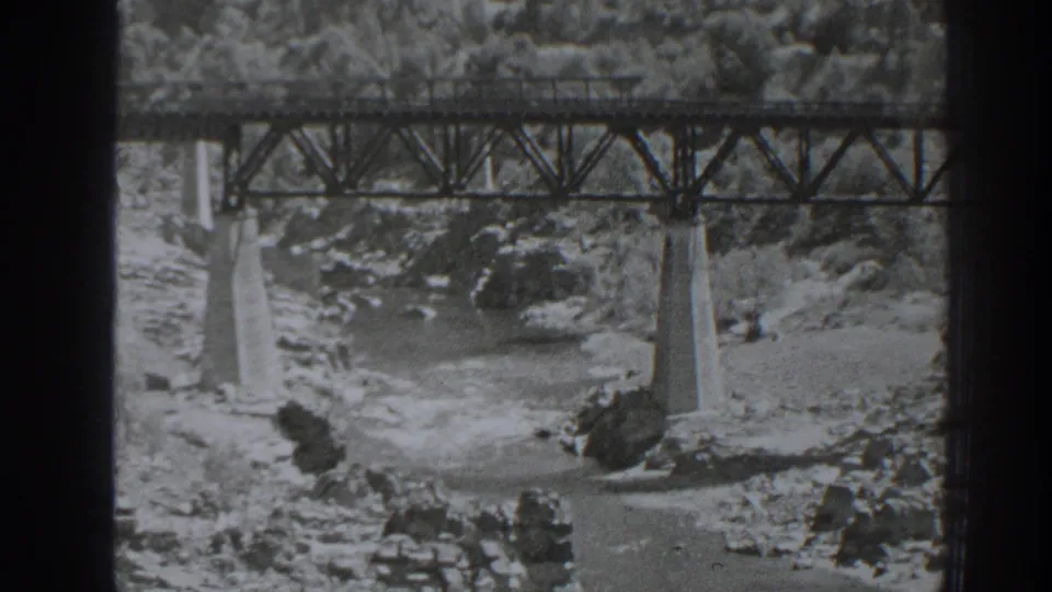 1938 Oroville frame with steel bridge trusses above concrete piers and rushing water in the rocky channel.