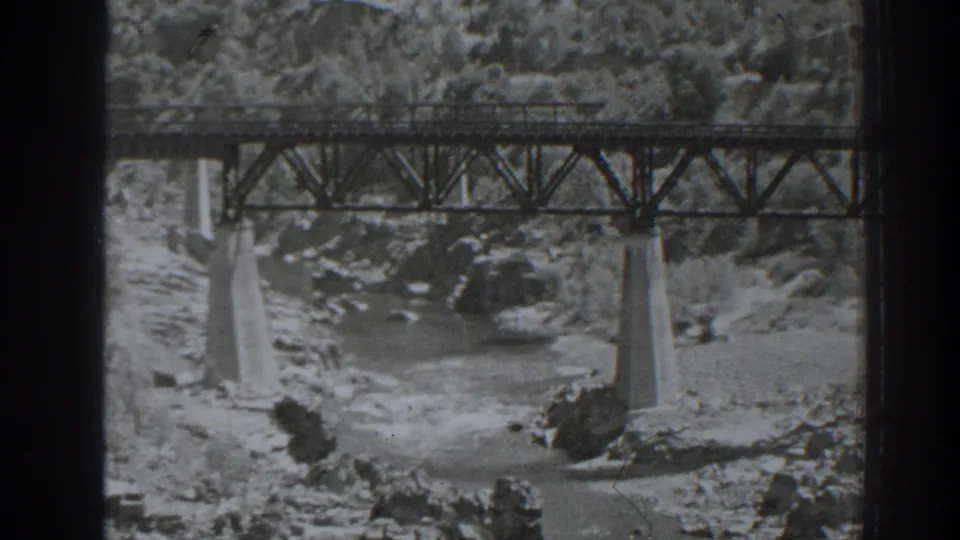 1938 Oroville, California home-movie frame showing a steel truss bridge on concrete piers above a rocky river channel.