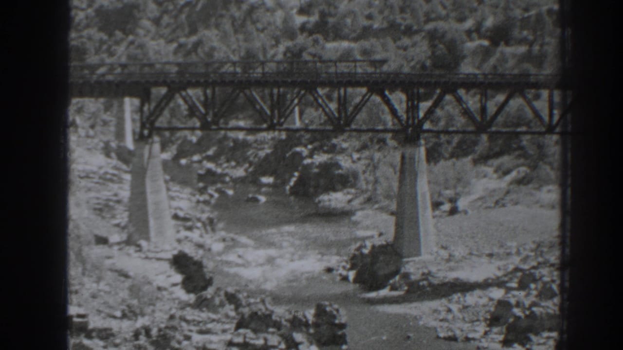A second view of the Oroville-area bridge shows the truss deck, concrete piers, river rocks, and wooded slope behind it.