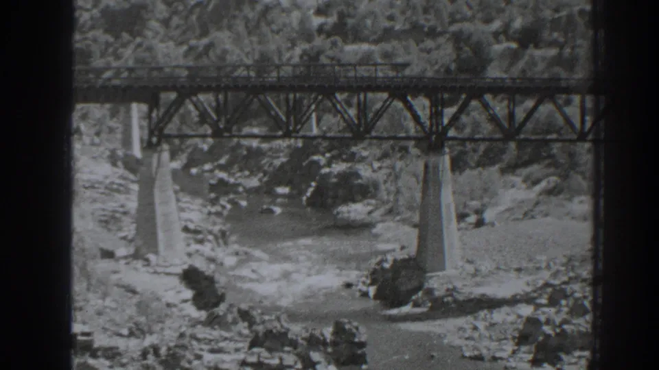 A second view of the Oroville-area bridge shows the truss deck, concrete piers, river rocks, and wooded slope behind it.