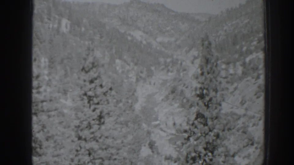 A soft 1938 home-movie view of the Oroville-area mountain landscape, with trees, slopes, and a pale channel or road through the valley.