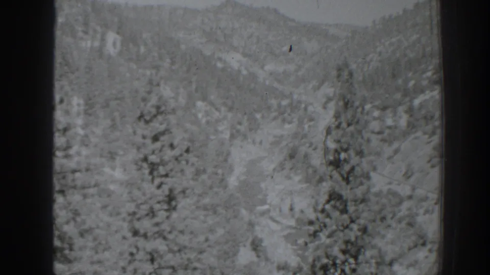 Black-and-white 1938 8mm frame of a snow-dusted pine valley near Oroville, California, with a distant wooded ridge.