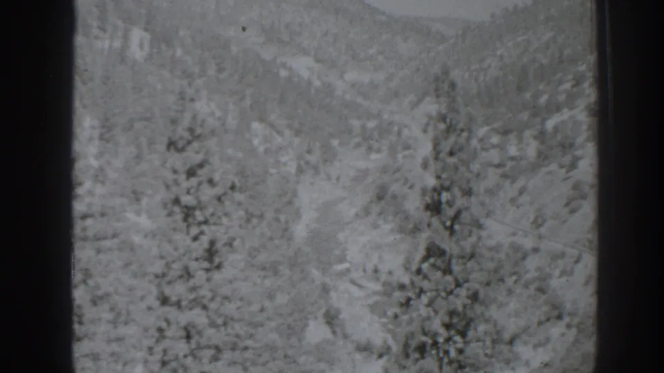Black-and-white 8mm view of a snowy pine-covered valley in the Oroville, California area, with hills rising in the background.