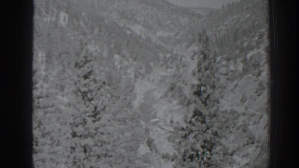 Black-and-white home-movie frame of a snow-dusted pine valley and wooded hills, identified by metadata as Oroville, California in 1938.