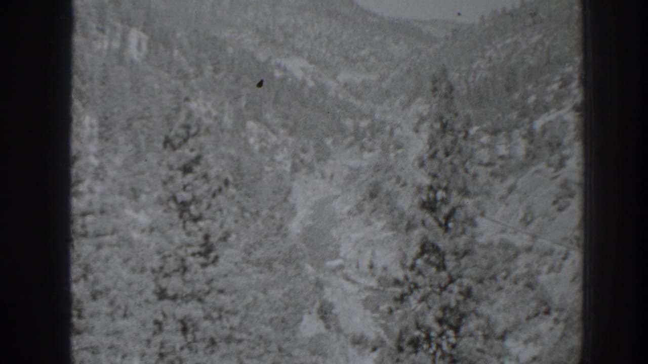 Snowy mountain valley with pine trees and distant ridgelines.