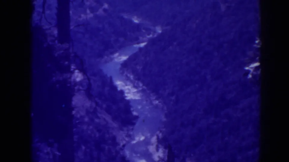 Blue-tinted 1938 Oroville 8mm frame showing a river bend below dense forested slopes and dark film edges.