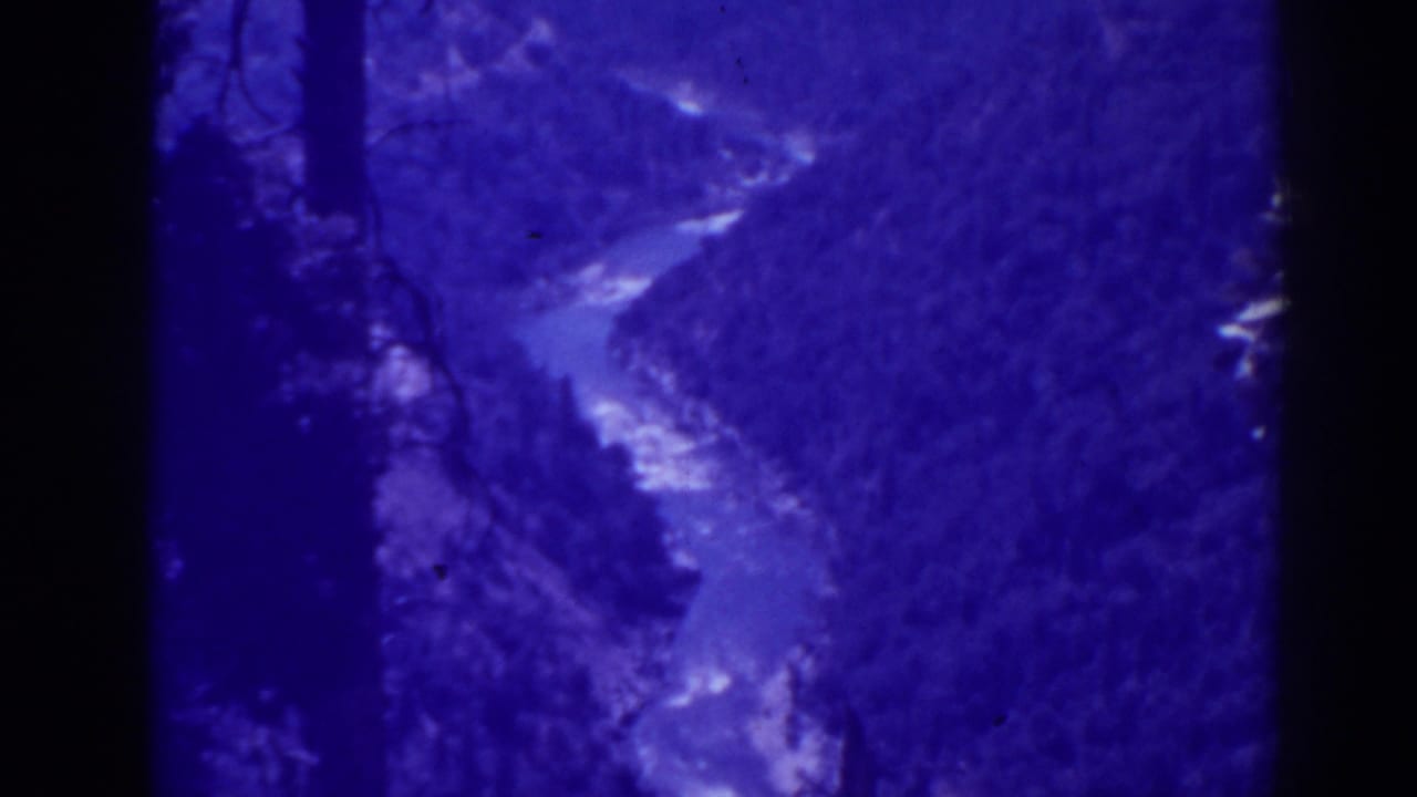 Blue-tinted view of a winding river through a wooded mountain valley.