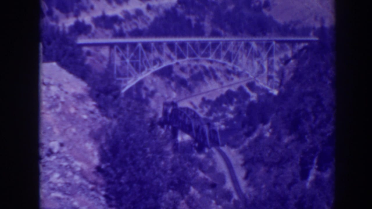 1938 Oroville, California home-movie frame showing a steel truss bridge above a rugged canyon and tree-covered slope.