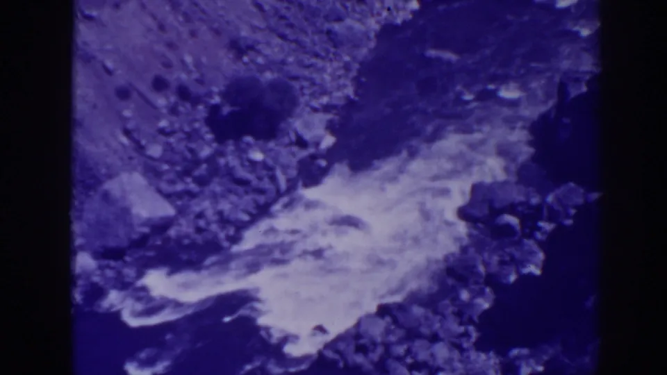 1938 Oroville creek footage shows bright running water crossing a shadowed rock bed.