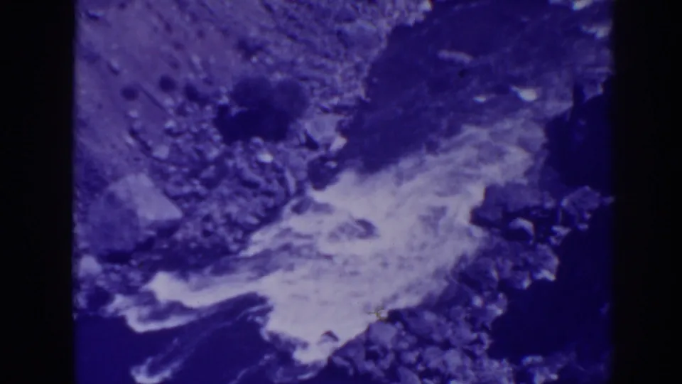 Close 8mm view of Oroville creek water flowing over stones, with blur and shifted color from the film scan.